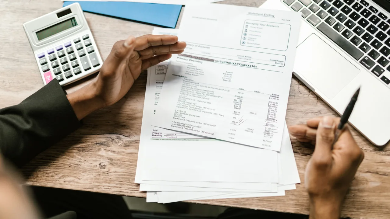 Manos revisando extractos bancarios junto a una calculadora