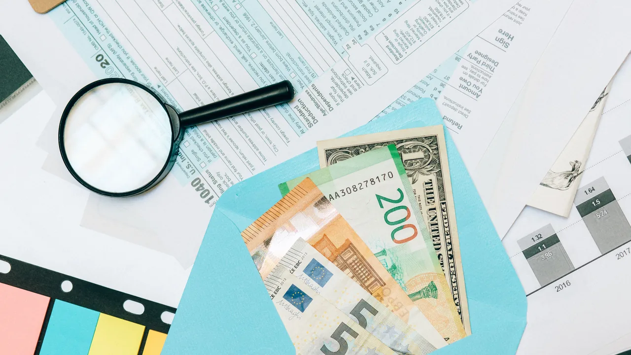 Documentos tributarios y billetes de euro junto a una lupa