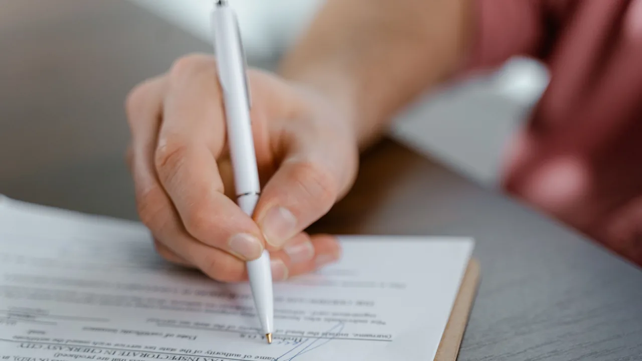 Mano escribiendo con bolígrafo sobre un documento en blanco