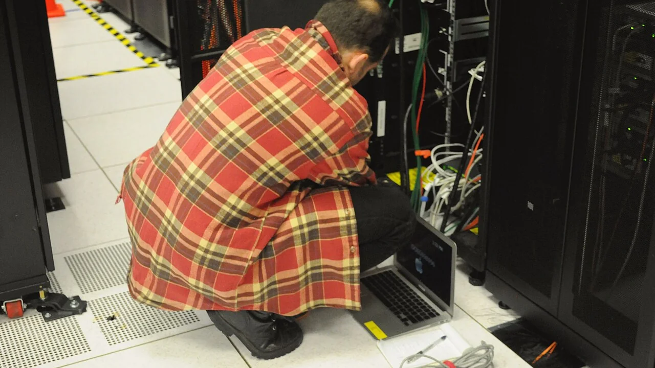 Técnico con un portátil trabajando en un rack de servidores, la tarea de IT que parchea PHP detrás del cierre contable