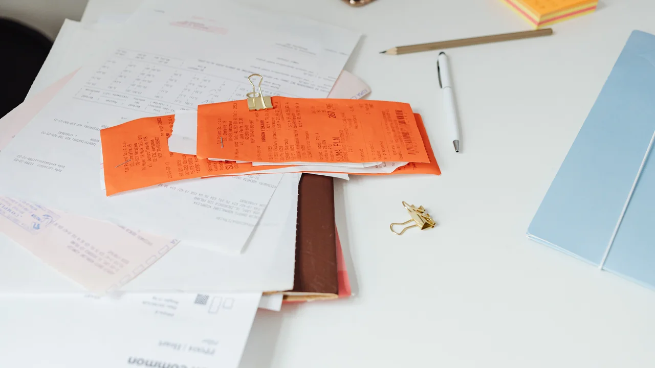 Escritorio de oficina con facturas impresas apiladas junto a un ordenador y una calculadora